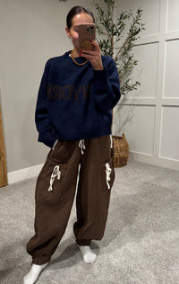 Person wearing a navy sweatshirt and brown pants taking a mirror selfie in a room.