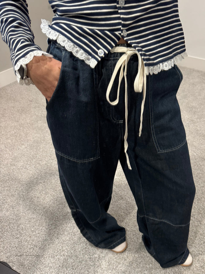 Person wearing dark blue jeans and a striped shirt on a tiled floor.
