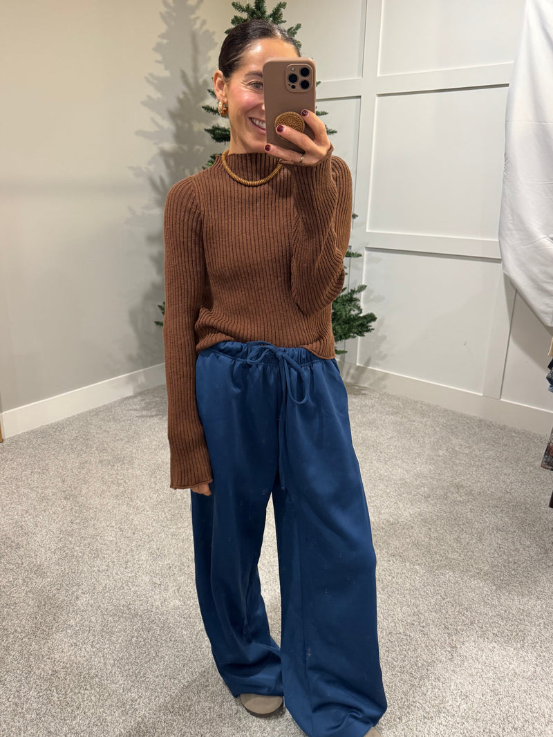 Person wearing a brown ribbed sweater and blue pants taking a mirror selfie.