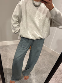 Person wearing a gray sweatshirt and blue pants standing in front of a mirror.